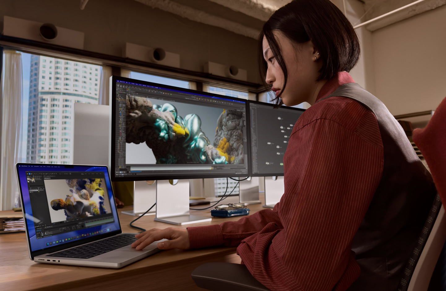 Henkilö työskentelee toimistoympäristössä MacBook-kannettavalla, johon on liitetty Studio Display XDR ‑näyttö Thunderbolt 5 ‑portin kautta