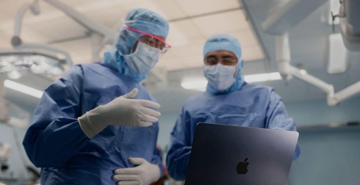 Två kirurger diskuterar något på skärmen på en MacBook Pro på operationsavdelningen.